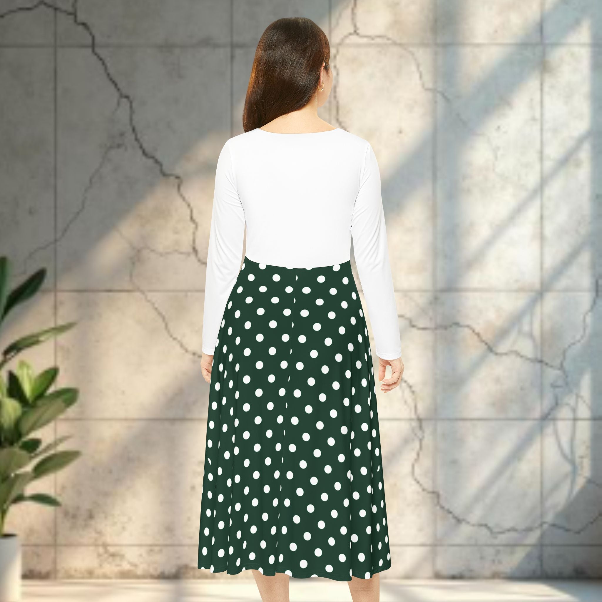 Woman wearing a white top and green polka dot skirt against a textured wall.