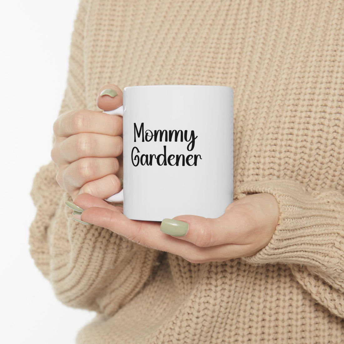 Person holding a white mug with 'Mommy Gardener' text, wearing a beige sweater.