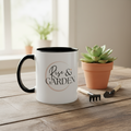 White mug with 'Rise & Garden' text on a wooden table with a potted succulent and gardening tools.