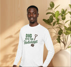 Man wearing a white long-sleeve shirt with 'Dig into the Holidays' text, standing in front of a plant.