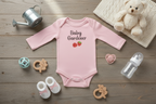 Pink baby onesie with 'Baby Gardener' text on a wooden surface with toys and a teddy bear.