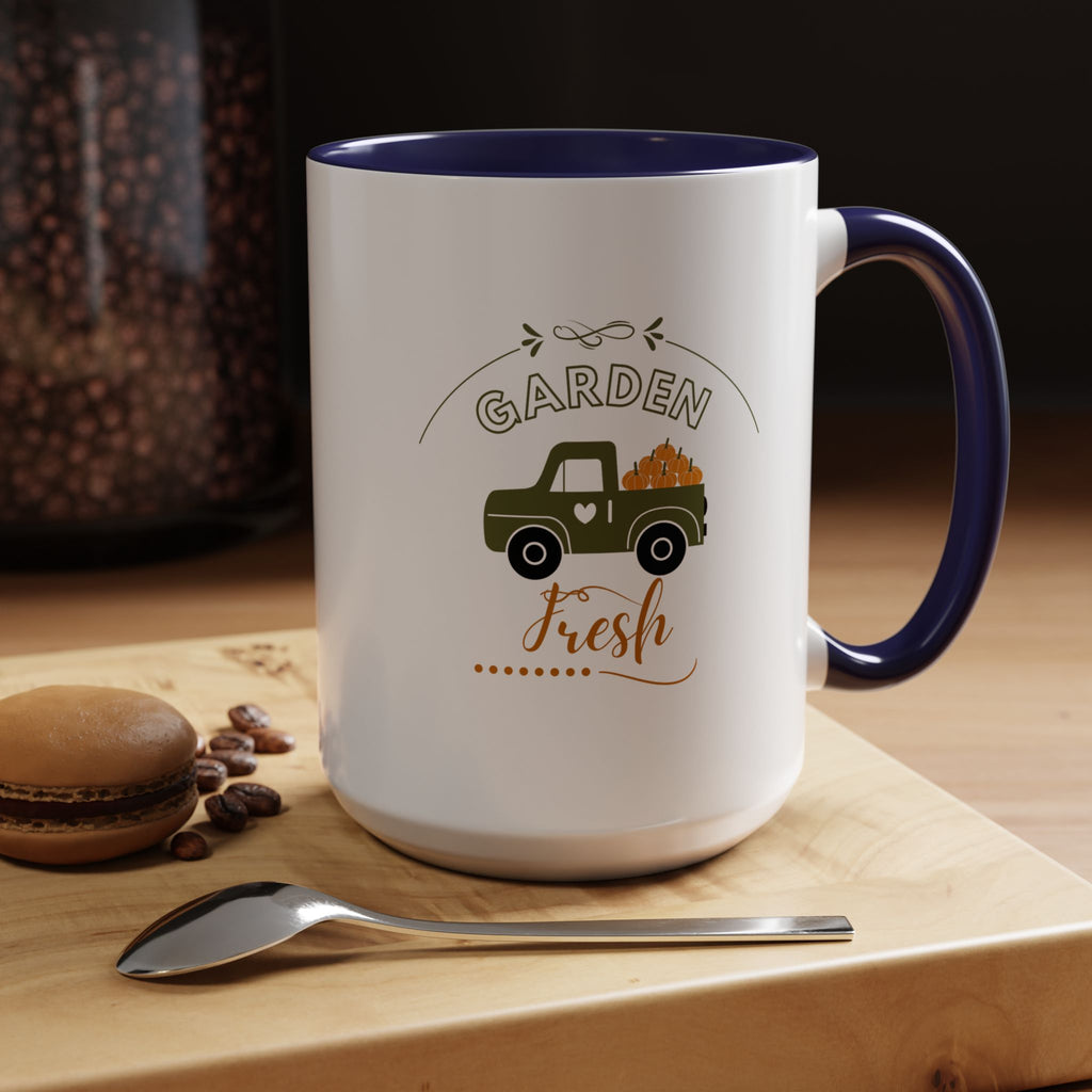 White mug with blue interior and handle, featuring a truck and 'Garden Fresh' text, on a wooden surface with coffee beans and a macaron.