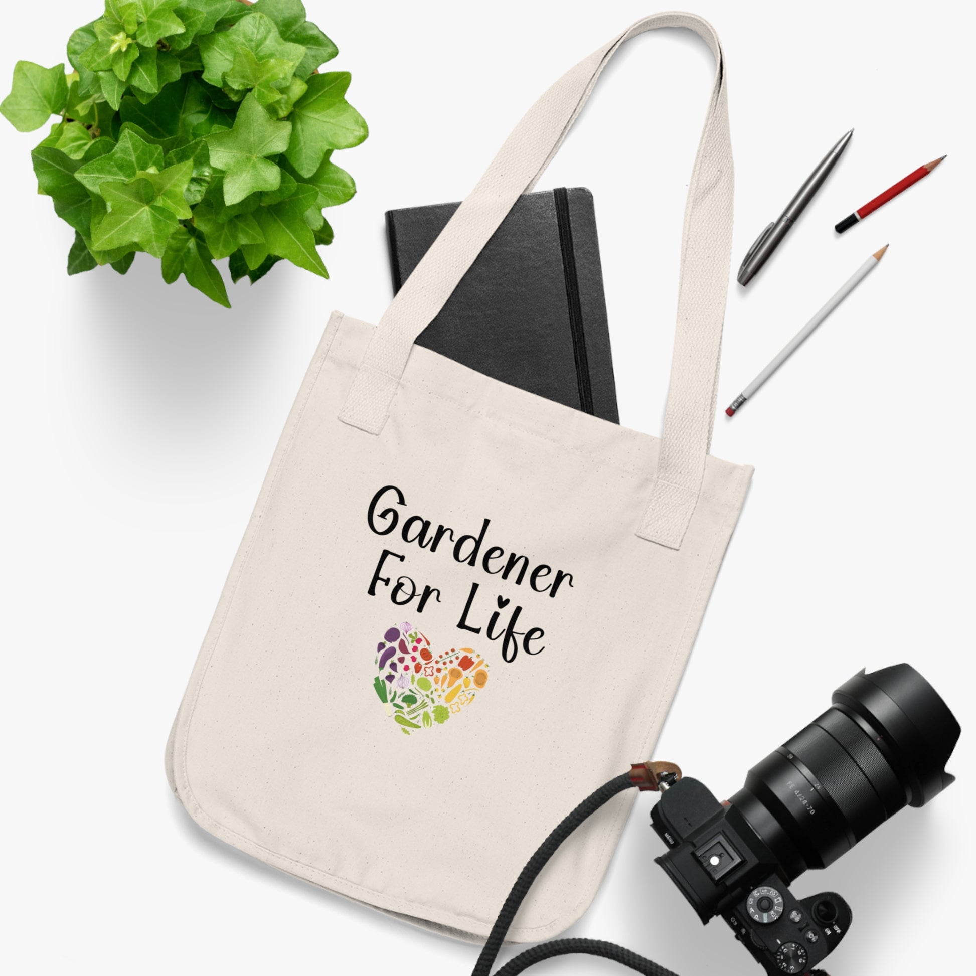 Beige tote bag with 'Gardener For Life' text and heart design, surrounded by stationery items on a white background.