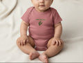 Pink baby onesie with green text and leaf design on a beige background