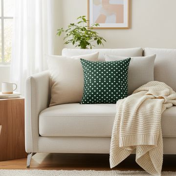 Beige sofa with a green polka dot pillow and beige blanket in a living room setting.