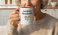 Person holding a mug with 'Gardening Grandma' text and floral design in a kitchen setting