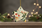 Decorative star ornament with floral pattern hanging on a wooden surface with pine branches and lights.