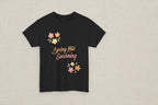 Black t-shirt with 'Spring Into Gardening' text and floral designs on a white background