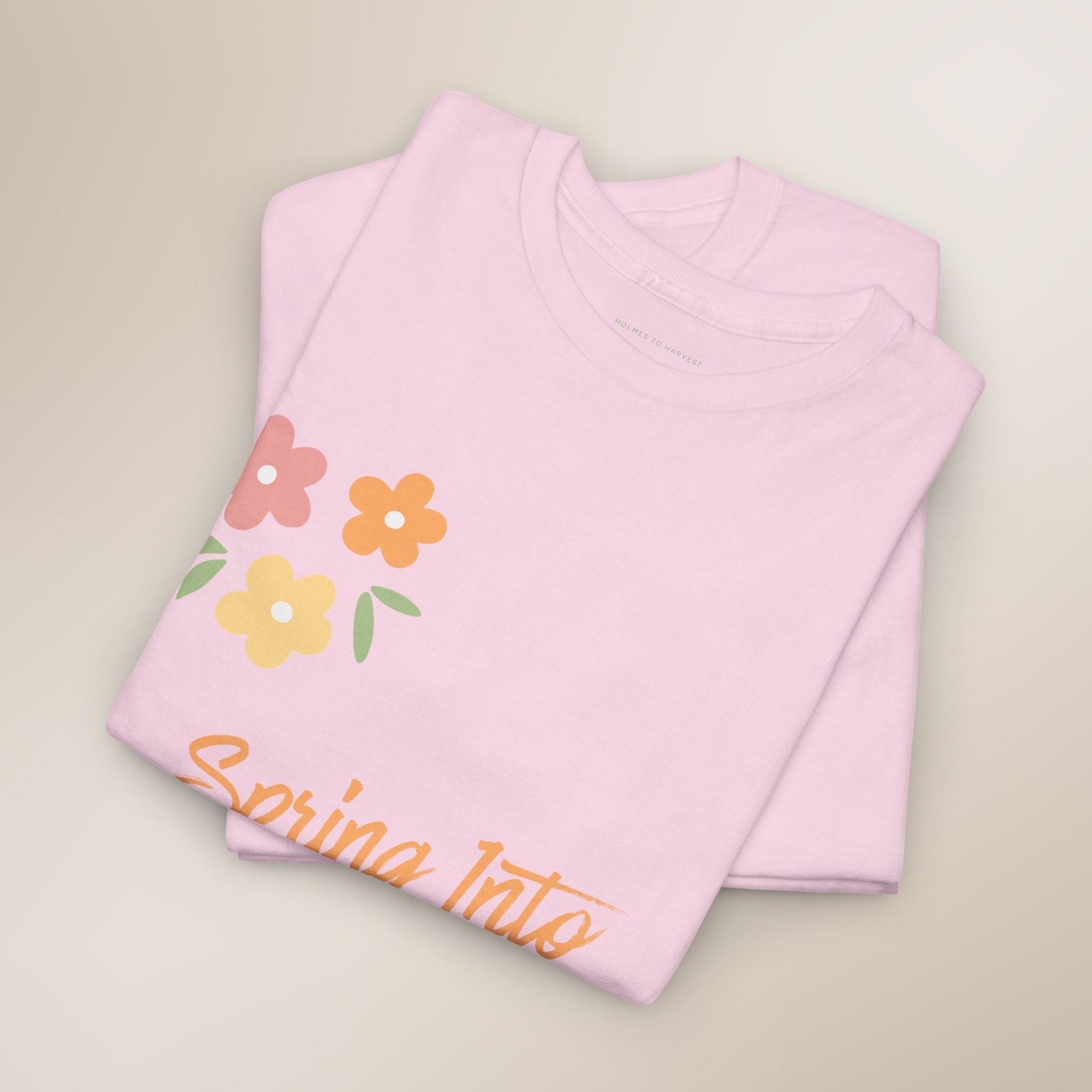 Folded pink shirt with floral design and 'Spring Into' text on a beige background