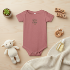Pink baby onesie with text on a wooden surface with toys and decor