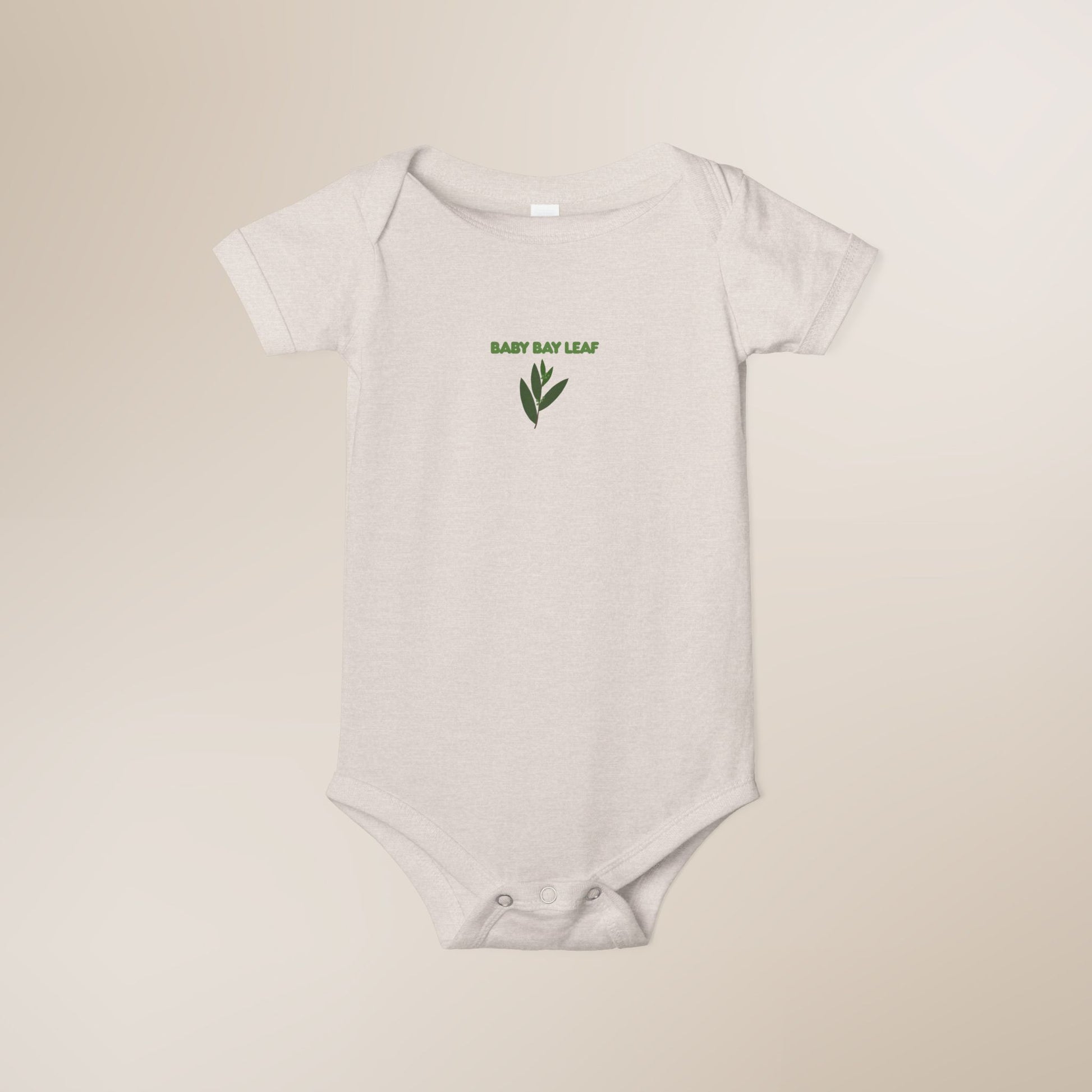 White baby onesie with green leaf design and text on a beige background