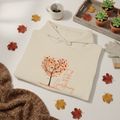 Beige hoodie with autumn-themed design on a table with fall leaves and gardening items.