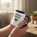 Person holding a mug with 'Grandpa Gardener' text and plant design in a home setting.