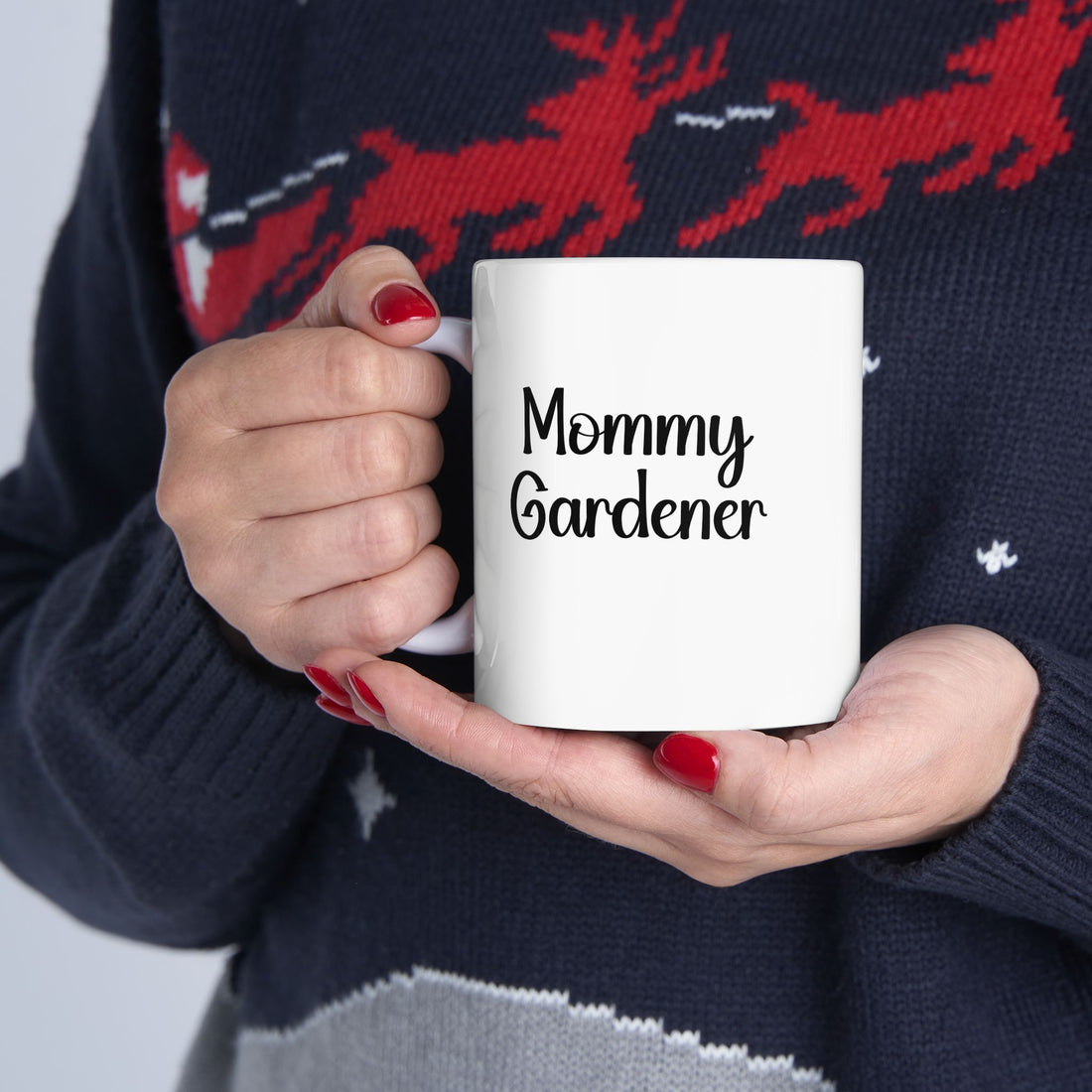 Person holding a mug with 'Mommy Gardener' text, wearing a navy sweater with red deer design.