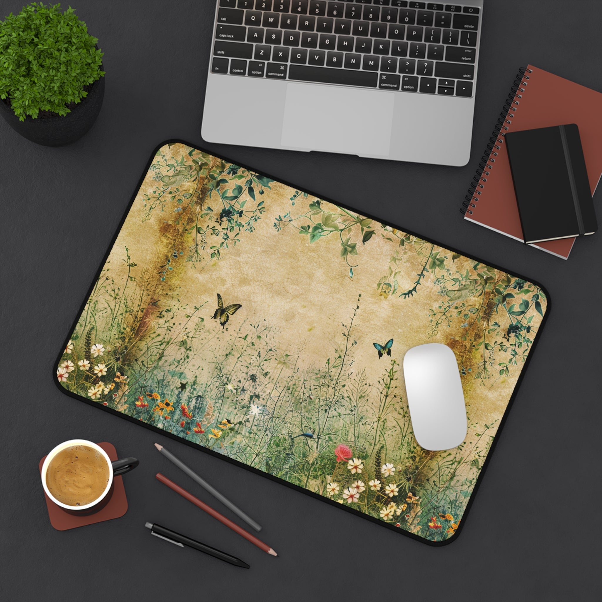 Desk setup with a floral mouse pad, laptop, notebook, and coffee cup on a dark surface.