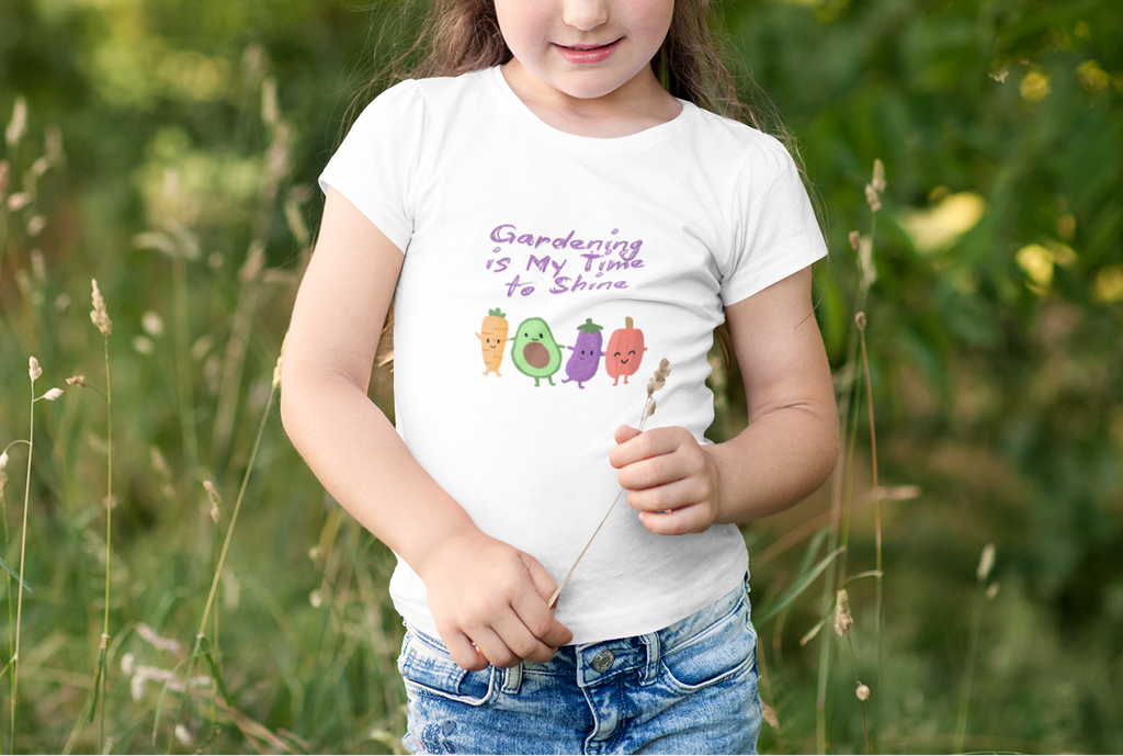 Young girl in a white t-shirt with gardening text and graphics standing in a field.