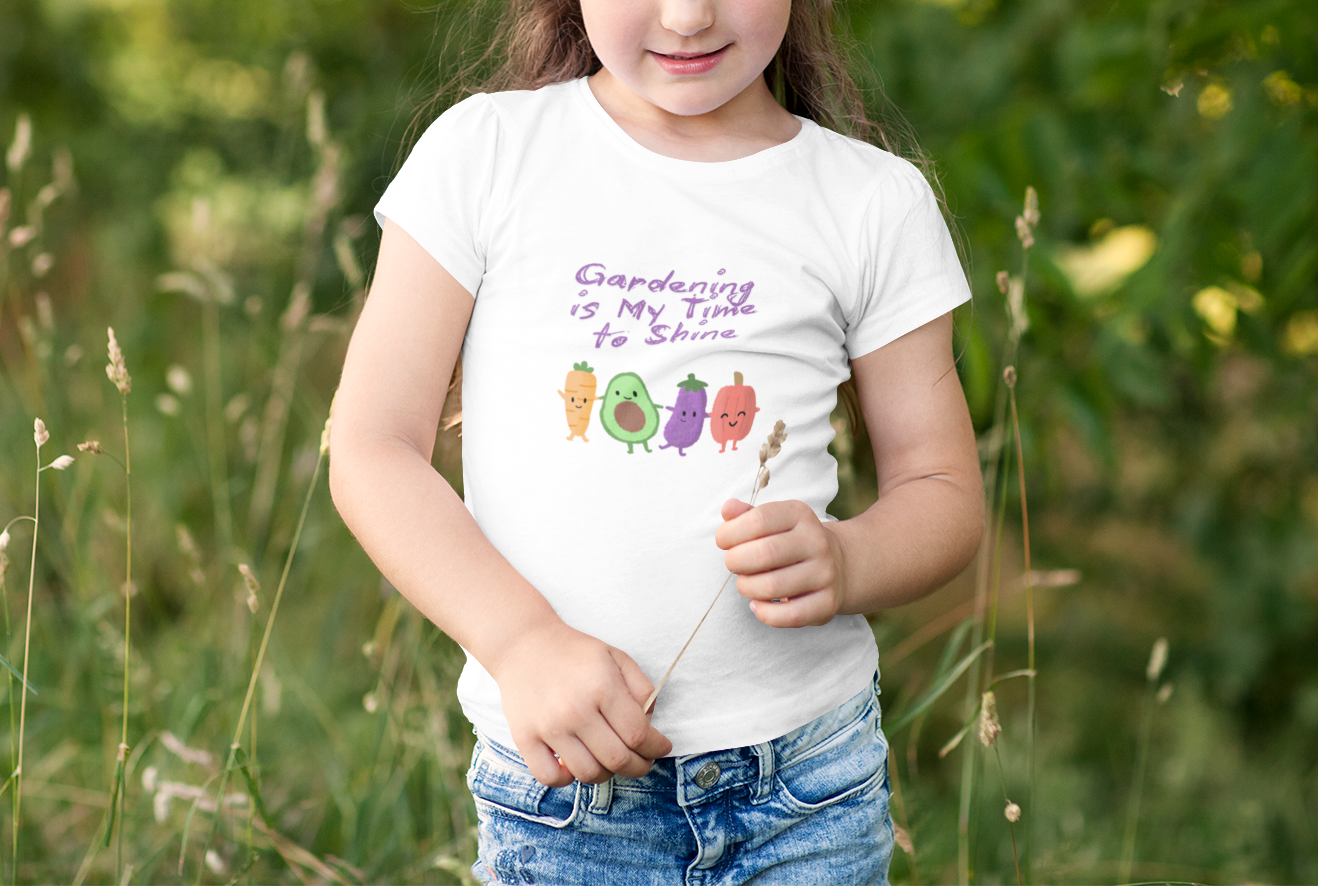 Young girl in a white t-shirt with gardening text and graphics standing in a field.