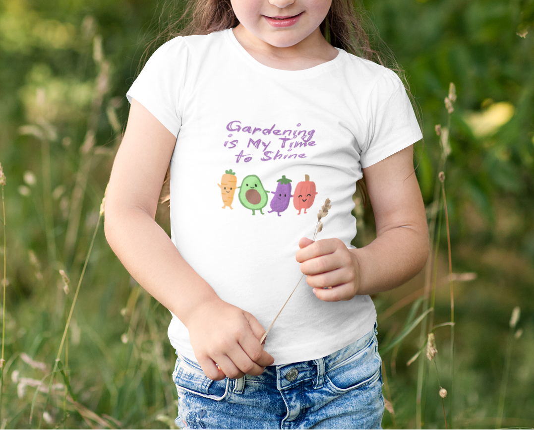 Child wearing a white t-shirt with gardening-themed design and text, standing in a grassy field.