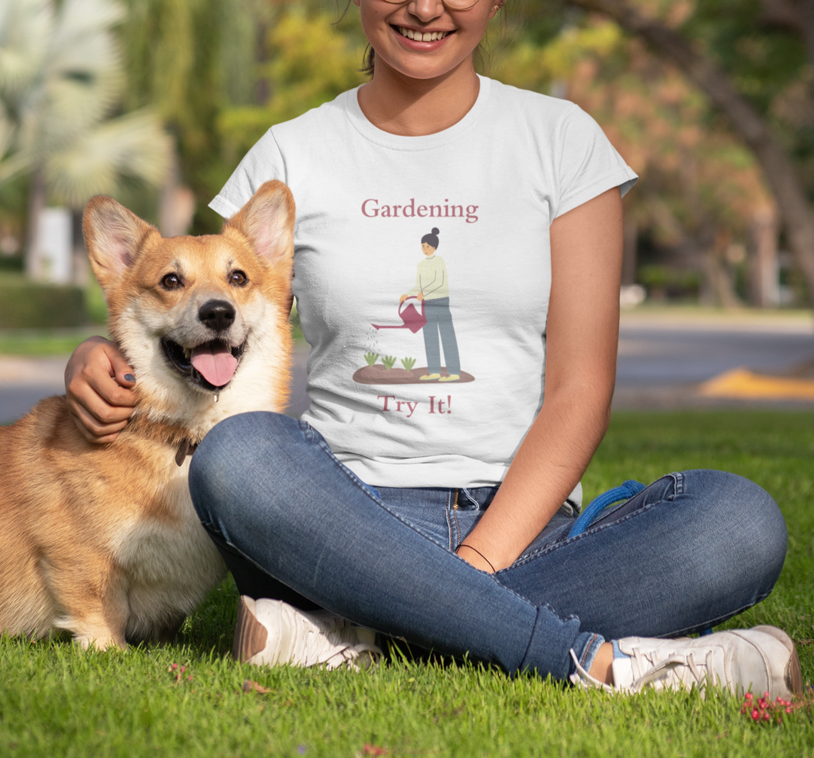 Person sitting on grass with a dog, wearing a t-shirt with a gardening graphic.