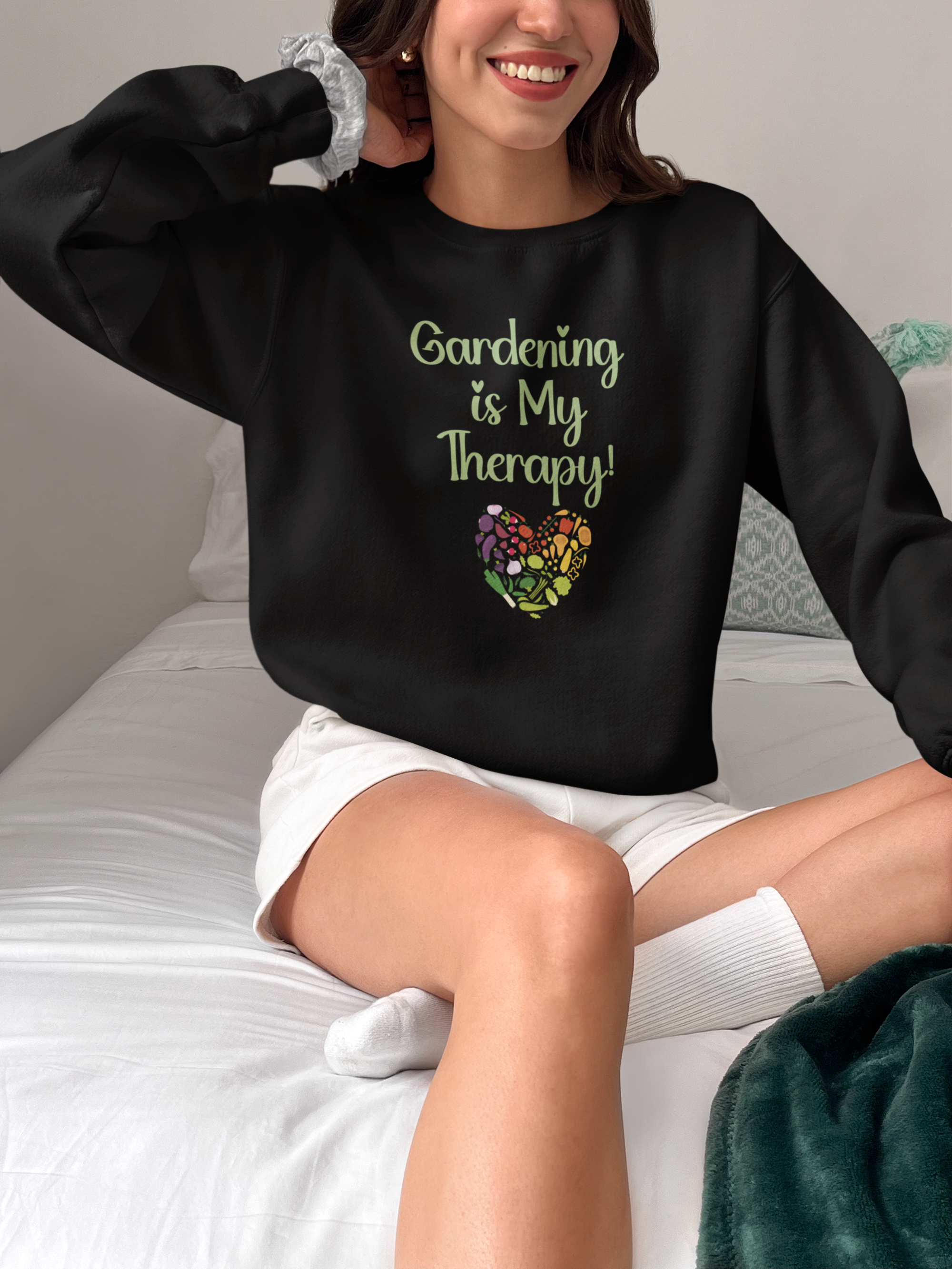 Person wearing a black sweatshirt with 'Gardening is My Therapy!' text and floral design, sitting on a bed.
