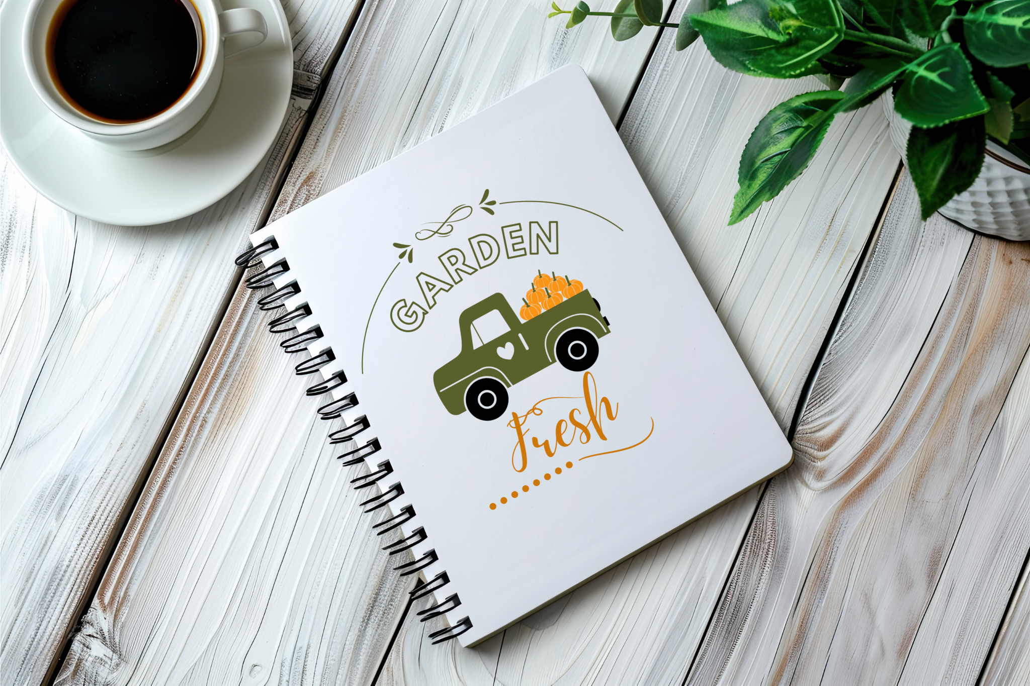 Notebook with a garden-themed design on a wooden surface with a cup of coffee and plant.