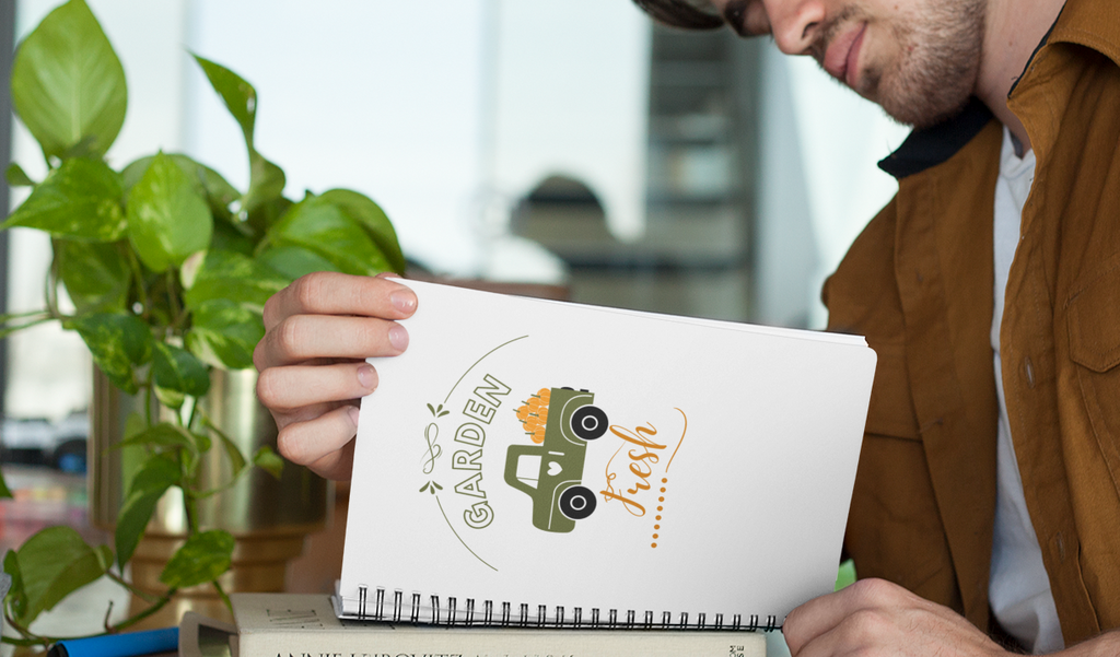Notebook with a garden-themed design on a wooden surface with a cup of coffee and plant.