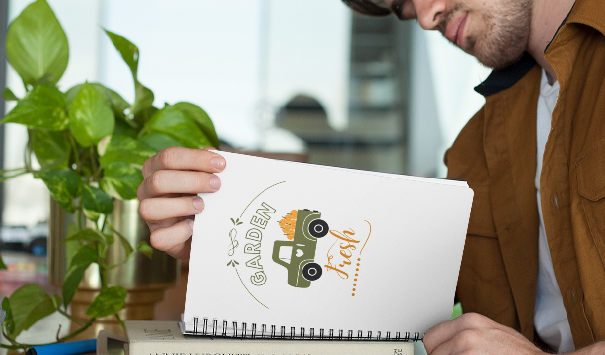 Notebook with a garden-themed design on a wooden surface with a cup of coffee and plant.