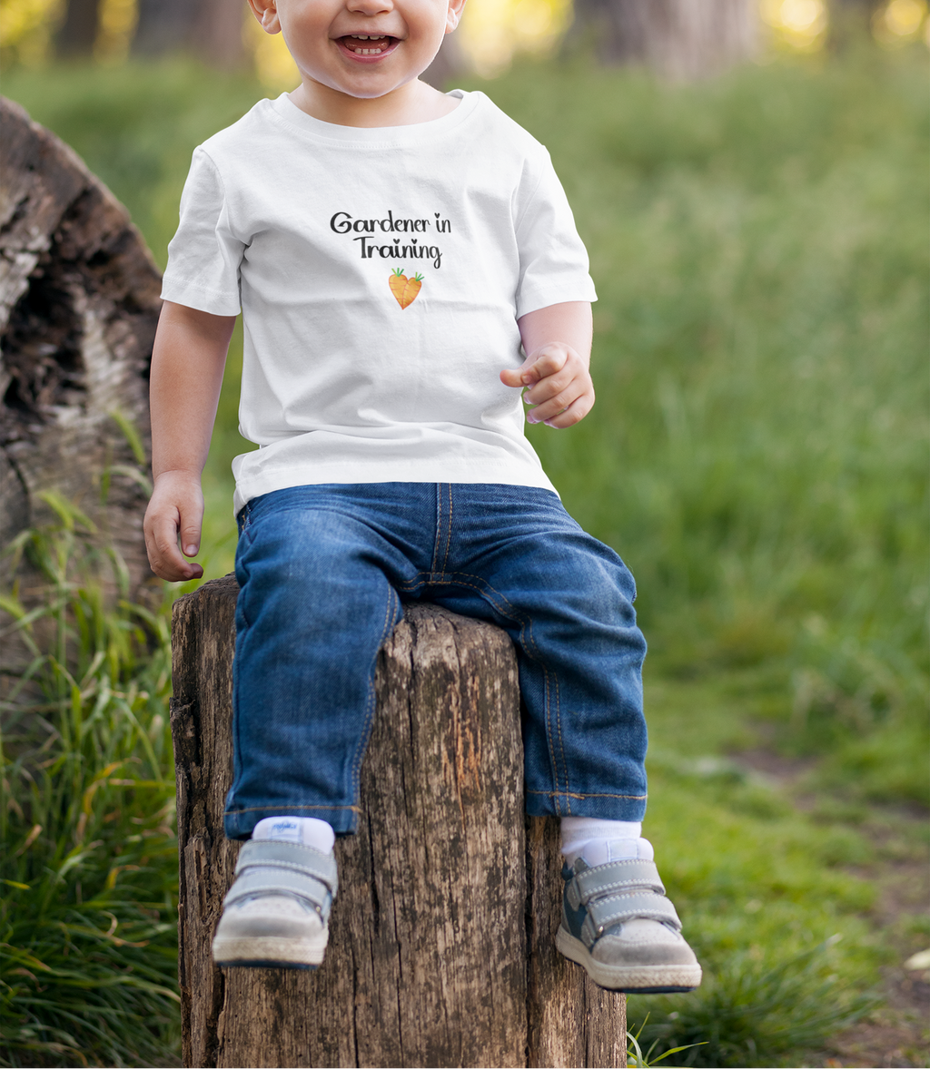 Child sitting on a log in a forest wearing a white t-shirt with text and graphics.