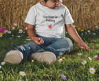 Child sitting in grass wearing a shirt with text and graphics