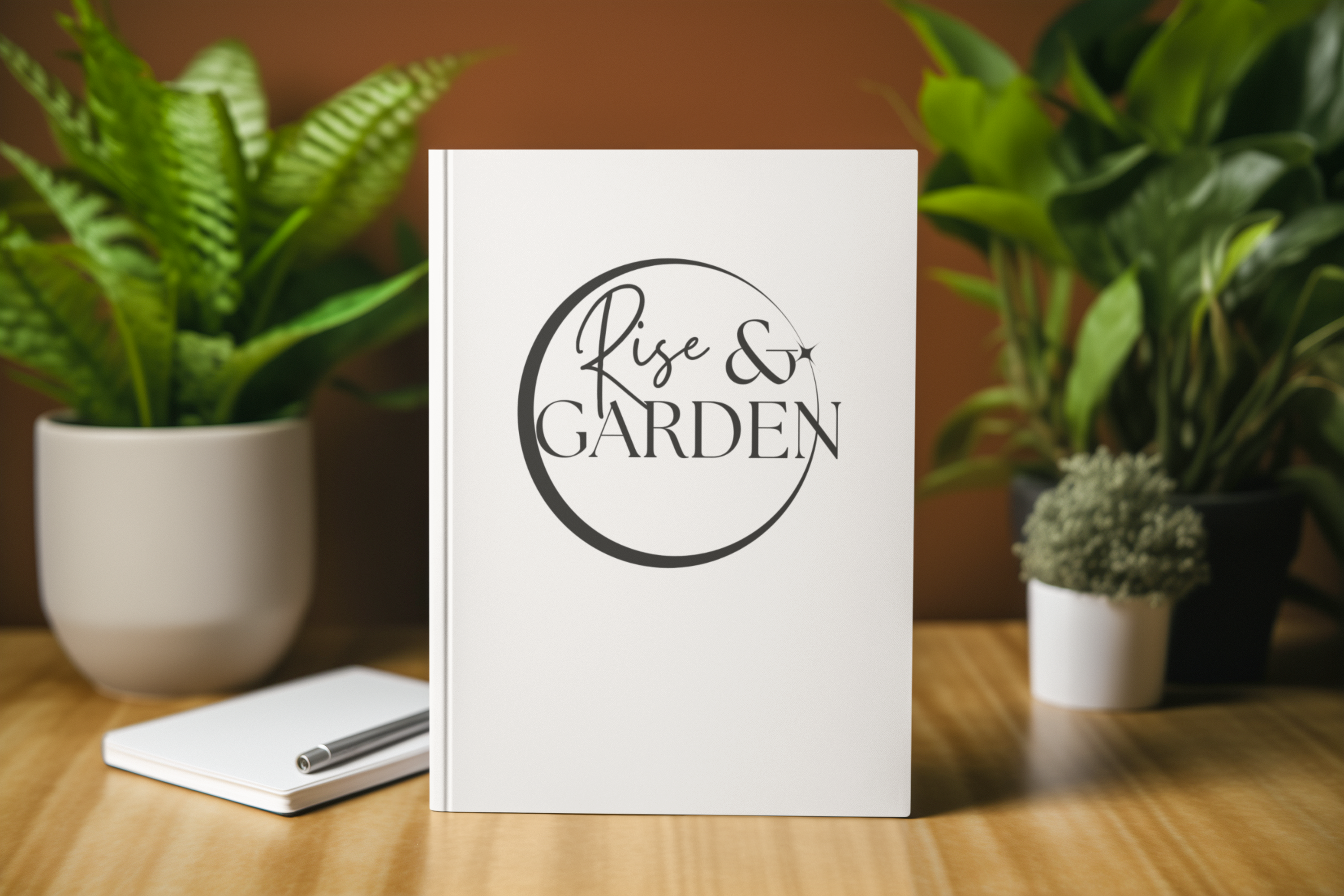 Notebook with 'Rise & Garden' logo on a wooden surface with plants in the background