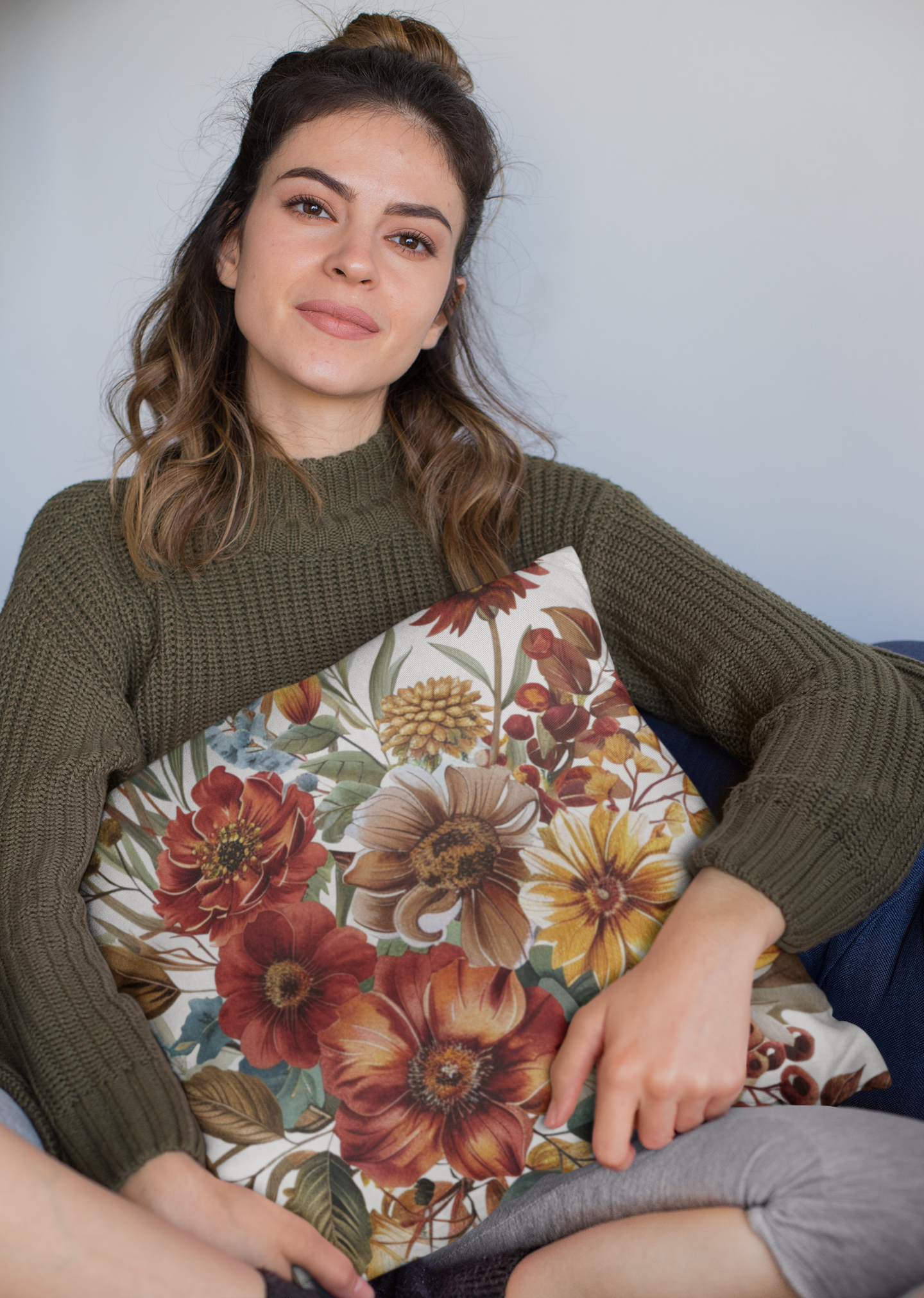 Woman holding a floral pillow against a plain background