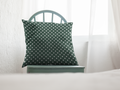 Green pillow with white polka dots on a white chair against a white curtain background