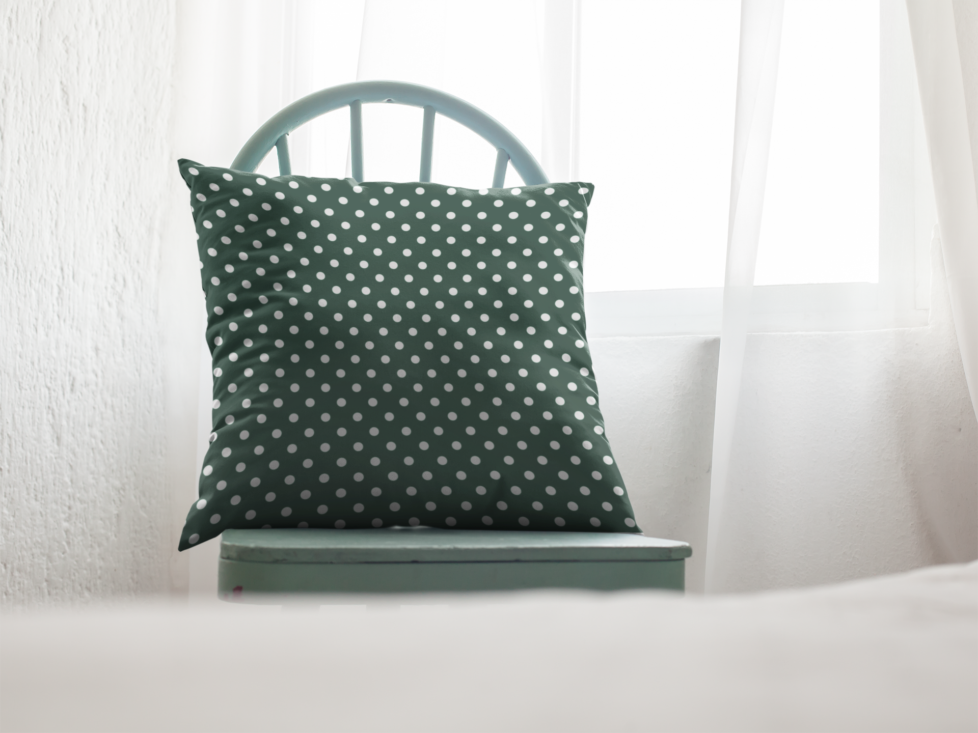 Green pillow with white polka dots on a white chair against a white curtain background