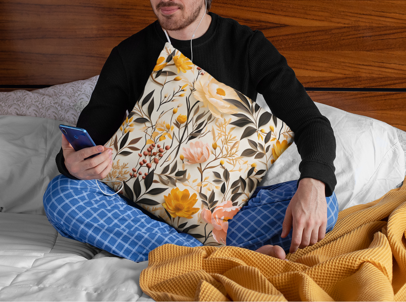 Man sitting on a bed using a phone with earphones, surrounded by pillows and a blanket.