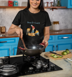 Woman in a kitchen wearing a black t-shirt with a graphic design, holding a pan.