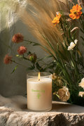 Candle with 'Garden Joy' branding in front of flowers and pampas grass.
