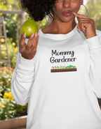 Woman wearing a white sweatshirt with 'Mommy Gardener' text, holding a green apple.