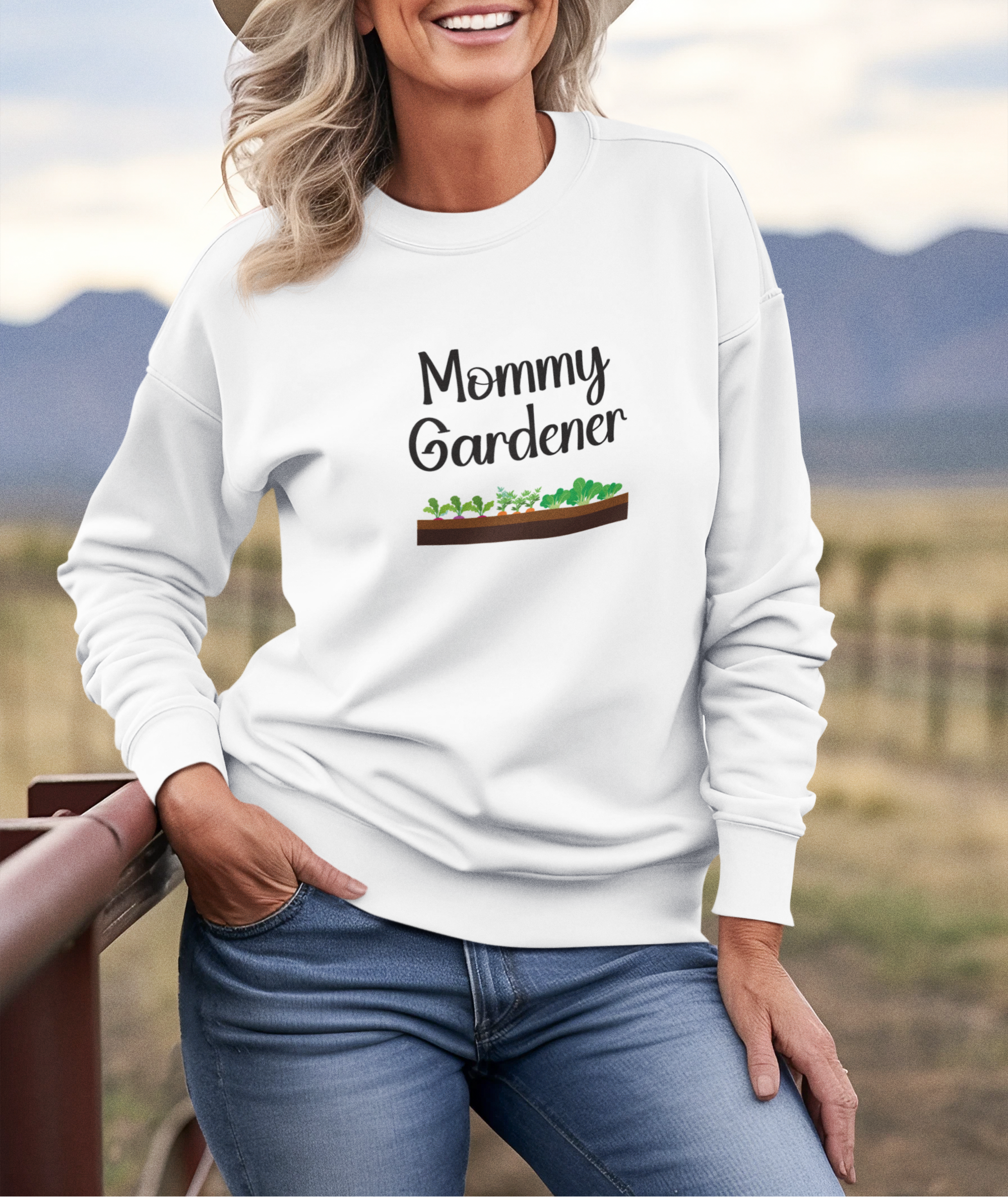 Woman wearing a white sweatshirt with 'Mommy Gardener' text and garden graphic, standing outdoors.