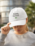 Person wearing a white cap with 'Mommy Gardener' text, outdoors.