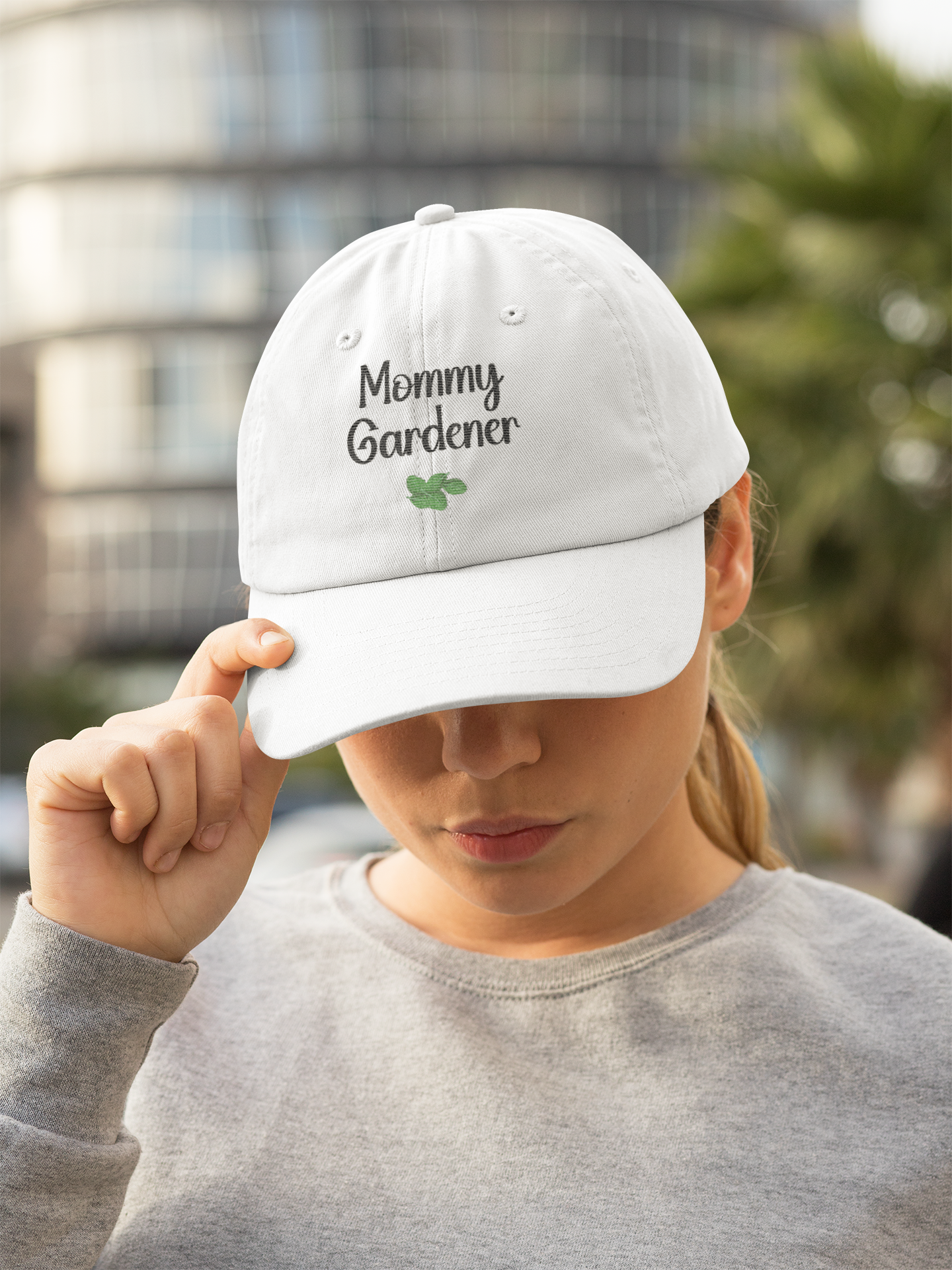Person wearing a white cap with 'Mommy Gardener' text, outdoors.