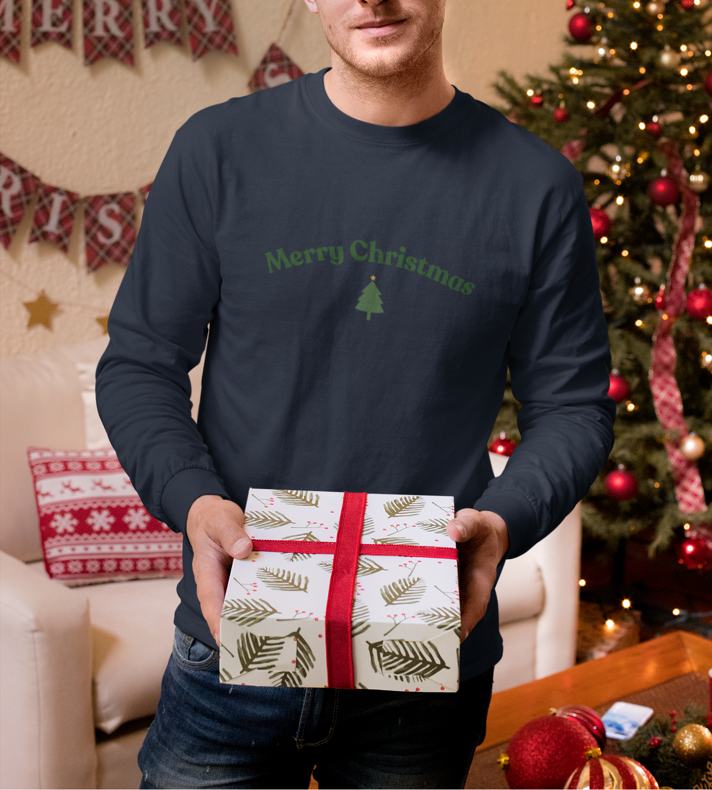 Man holding a gift box in front of a decorated Christmas tree and 'Merry Christmas' banner.