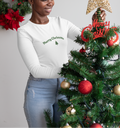 Woman decorating a Christmas tree with a gold star and red ornaments, wearing a 'Merry Christmas' sweater.