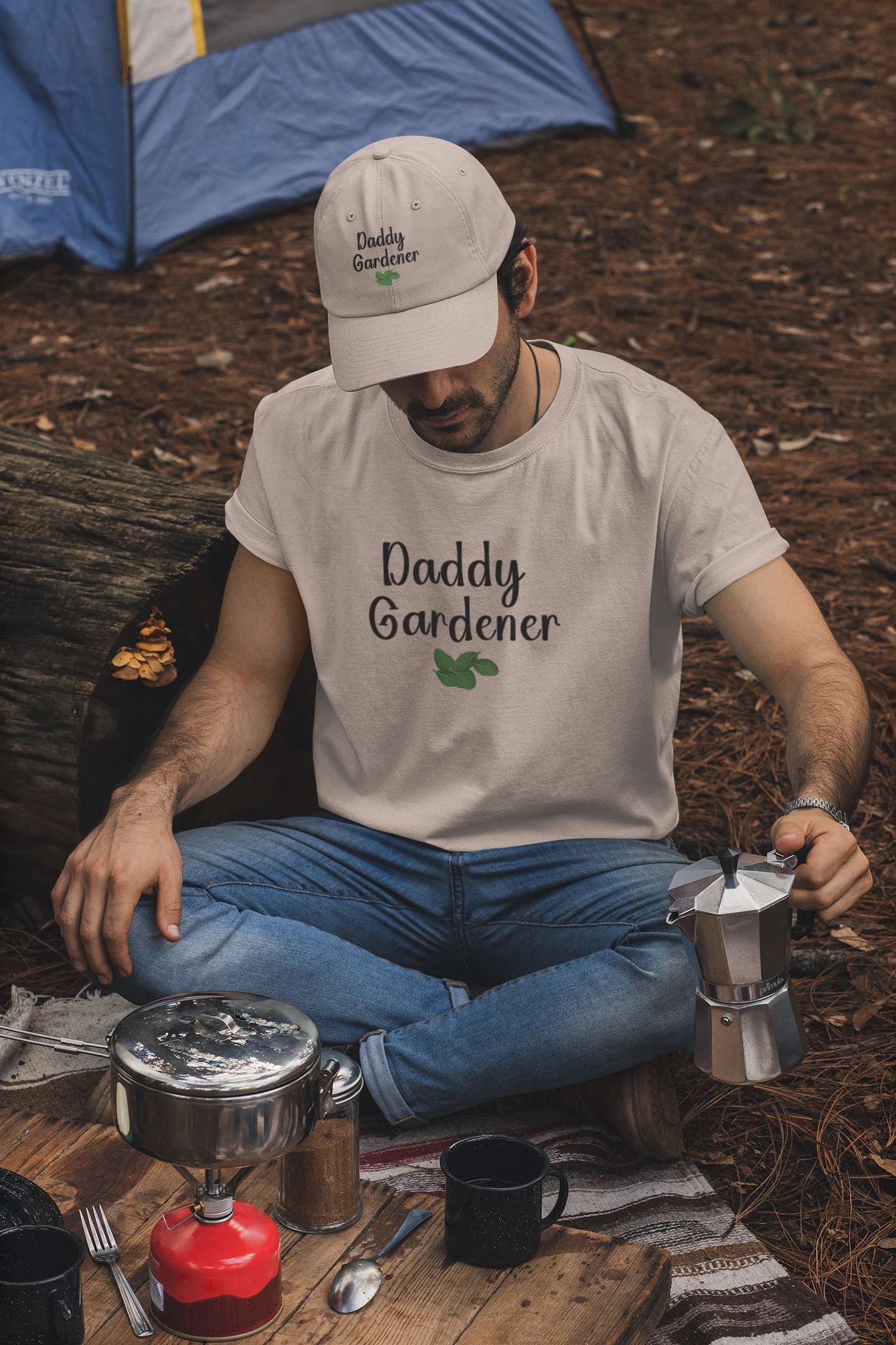 Man in 'Daddy Gardener' t-shirt sitting outdoors with camping gear and coffee equipment.