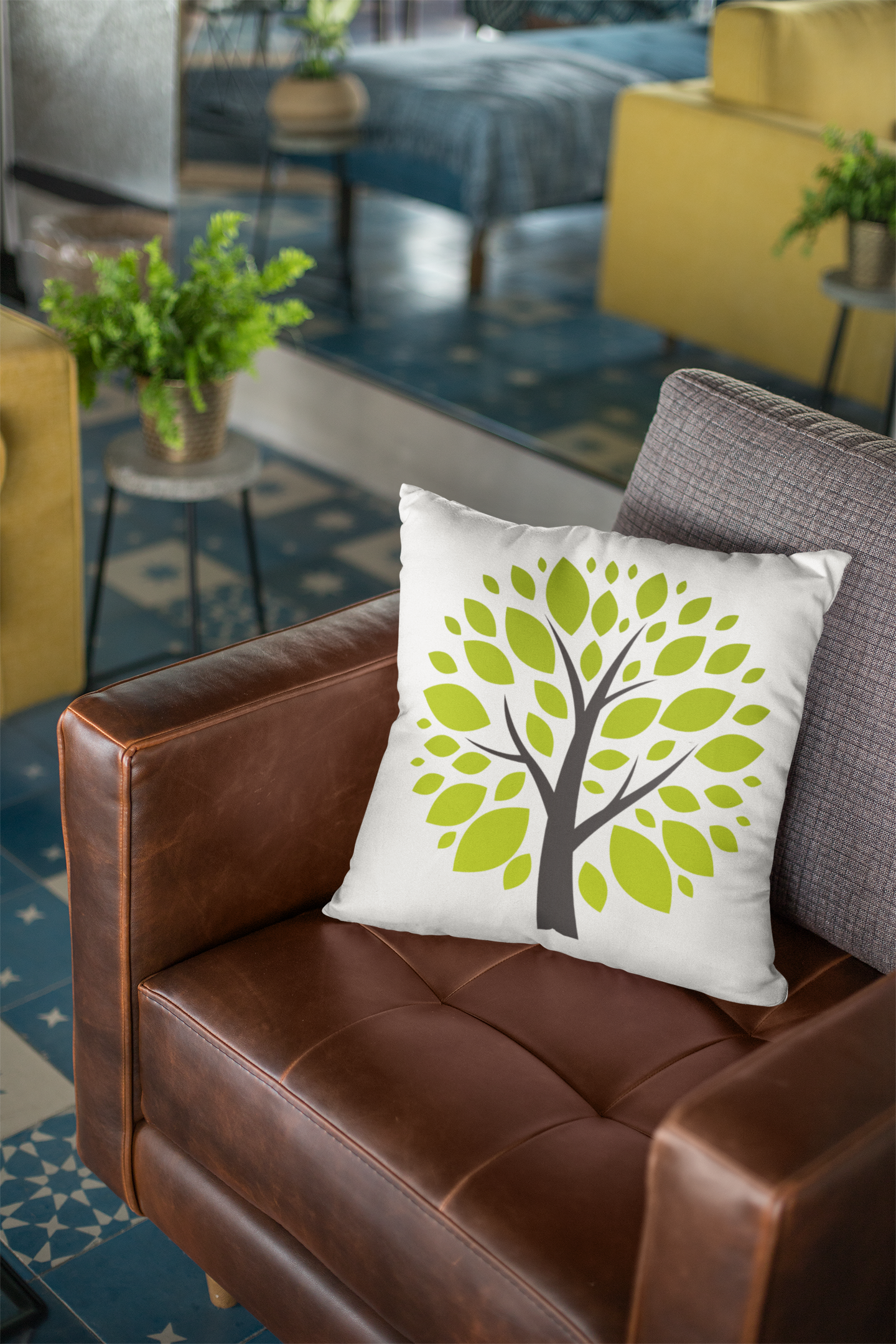 Decorative pillow with a tree design on a brown leather couch in a room with plants and furniture.