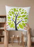White pillow with green leaf design held by hands against a blurred background