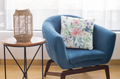 Blue armchair with a floral pillow next to a side table with a woven lantern, in a bright room.