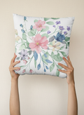 Floral-patterned pillow held by hands against a green and gray background