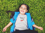 Child wearing a 'Gardener in Training' shirt lying on grass