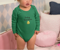 Child wearing a green 'Baby Gardener' onesie in a cozy room with pillows and a couch.