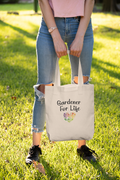 Person holding a tote bag with 'Gardener For Life' text in a grassy outdoor setting